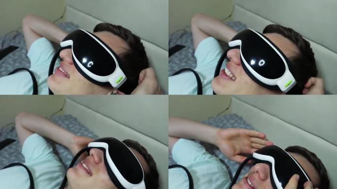 年轻有魅力的男人使用眼睛按摩器装置，躺在床上，拿着遥控器，特写
