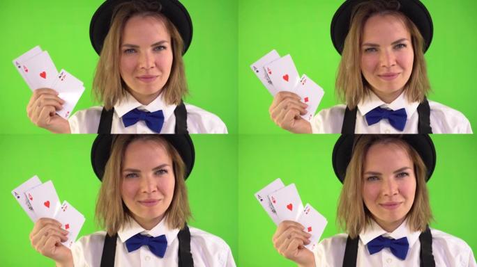 穿着白衬衫，帽子和领结的副主持人展示了扑克牌和微笑。四张王牌。绿色背景，chromakey