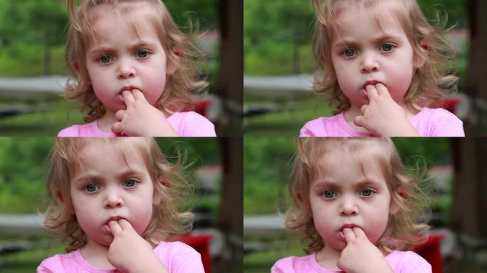 一个littel女孩吮吸两根手指并盯着相机的特写镜头