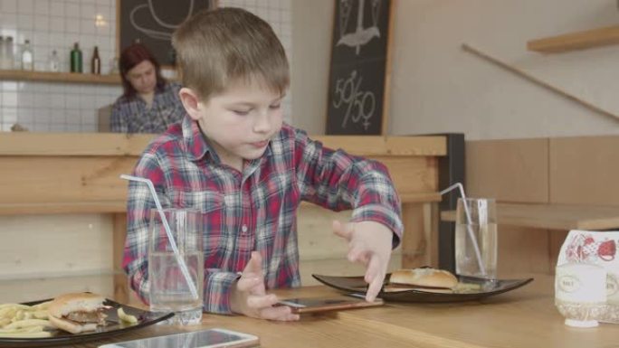 小男孩在咖啡馆吃饭时在手机上玩游戏