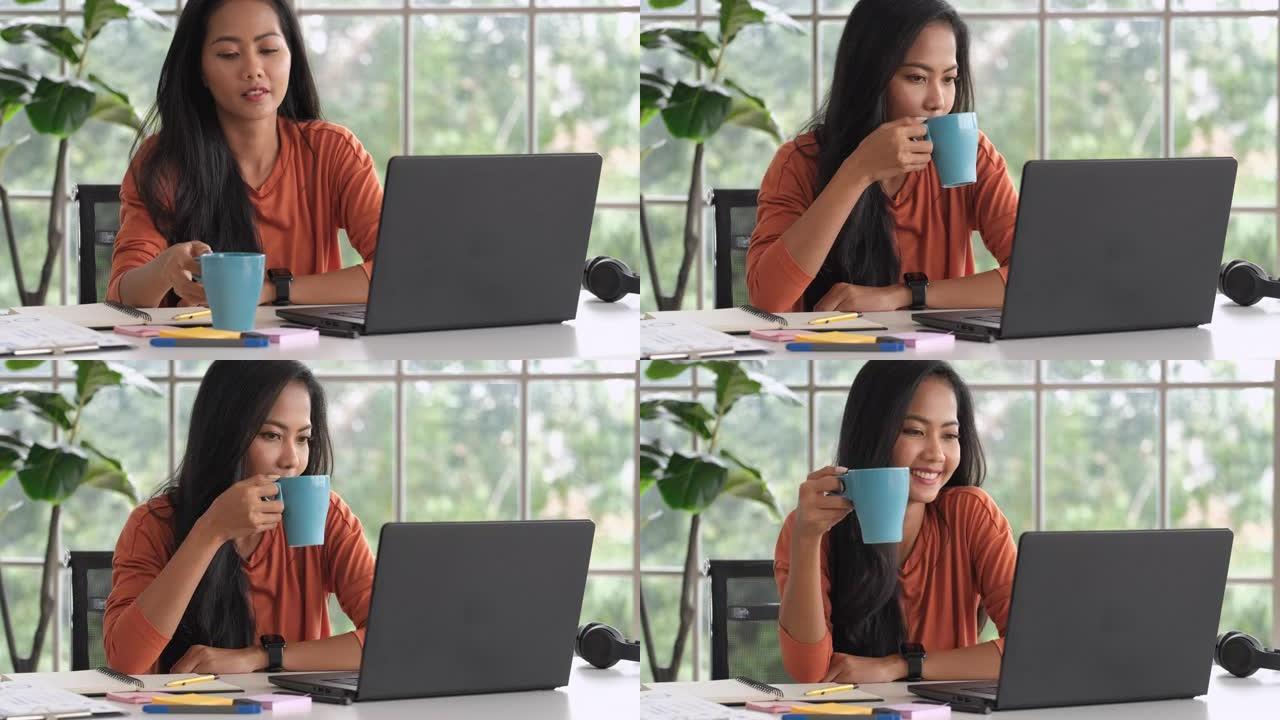亚洲女性在家工作，微笑着喝咖啡，同时用笔记本电脑在线工作。新的正常生活方式