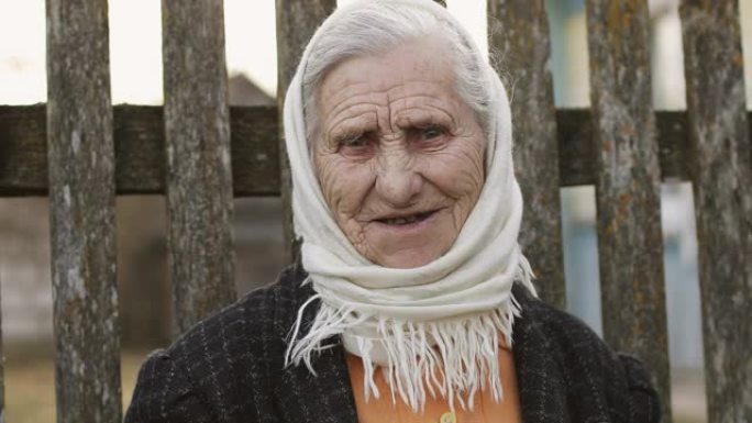 一位老女人的肖像，在旧篱笆的背景上，围巾上有深深的皱纹。