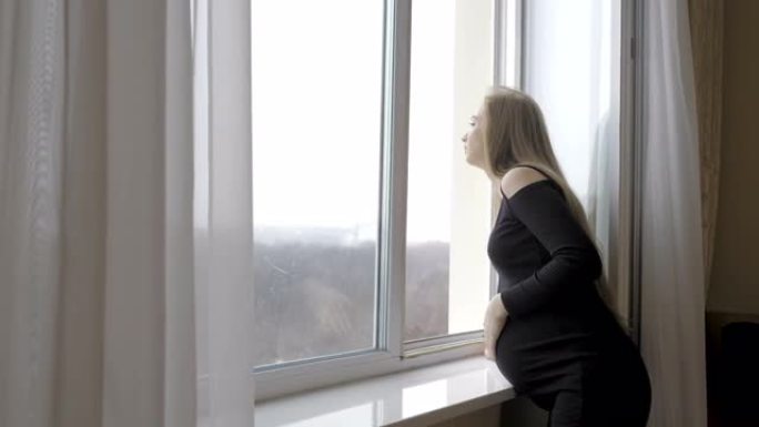 一个年轻孕妇站在窗边，抱着她的肚子