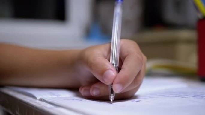 小学生用手柄用左手在笔记本上写字。在线家庭培训