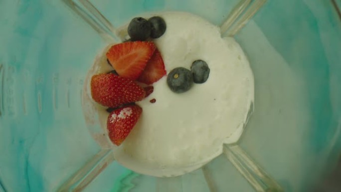 搅拌机内有许多浆果落入牛奶中。用搅拌机制作酸奶的场景。草莓和蓝莓以慢动作溅到搅拌机内的牛奶上。在阿里