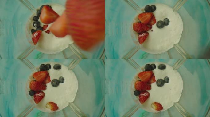 搅拌机内有许多浆果落入牛奶中。用搅拌机制作酸奶的场景。草莓和蓝莓以慢动作溅到搅拌机内的牛奶上。在阿里