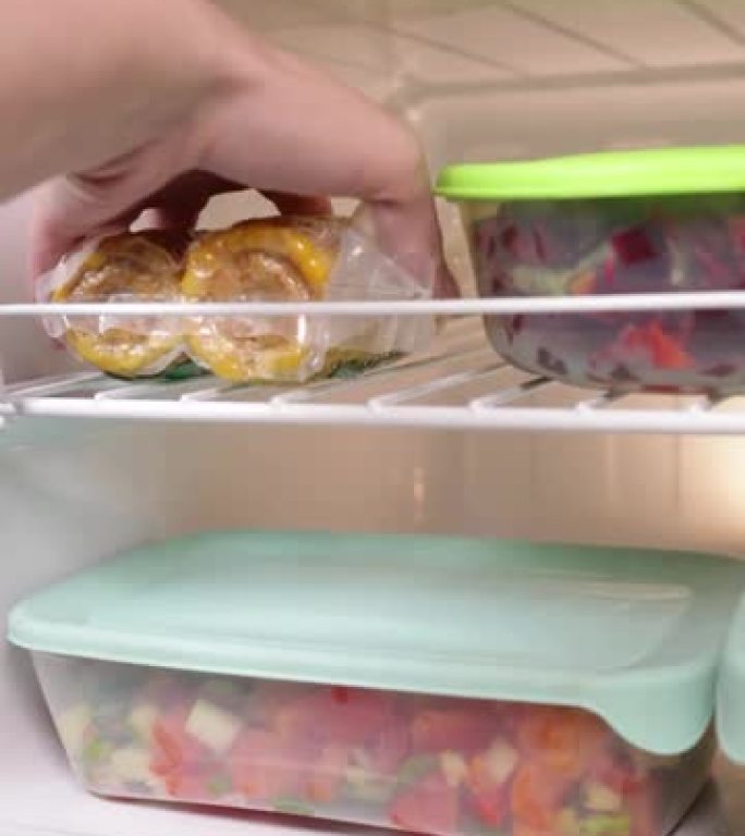 一个女人在真空的冰箱里得到玉米。冷冻蔬菜和水果，蘑菇，混合物，汤制剂。家庭烹饪用半成品。垂直视频