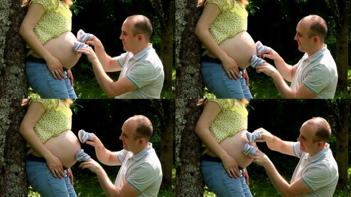 快乐老公男人玩小宝宝鞋在他怀孕的妻子女人肚子