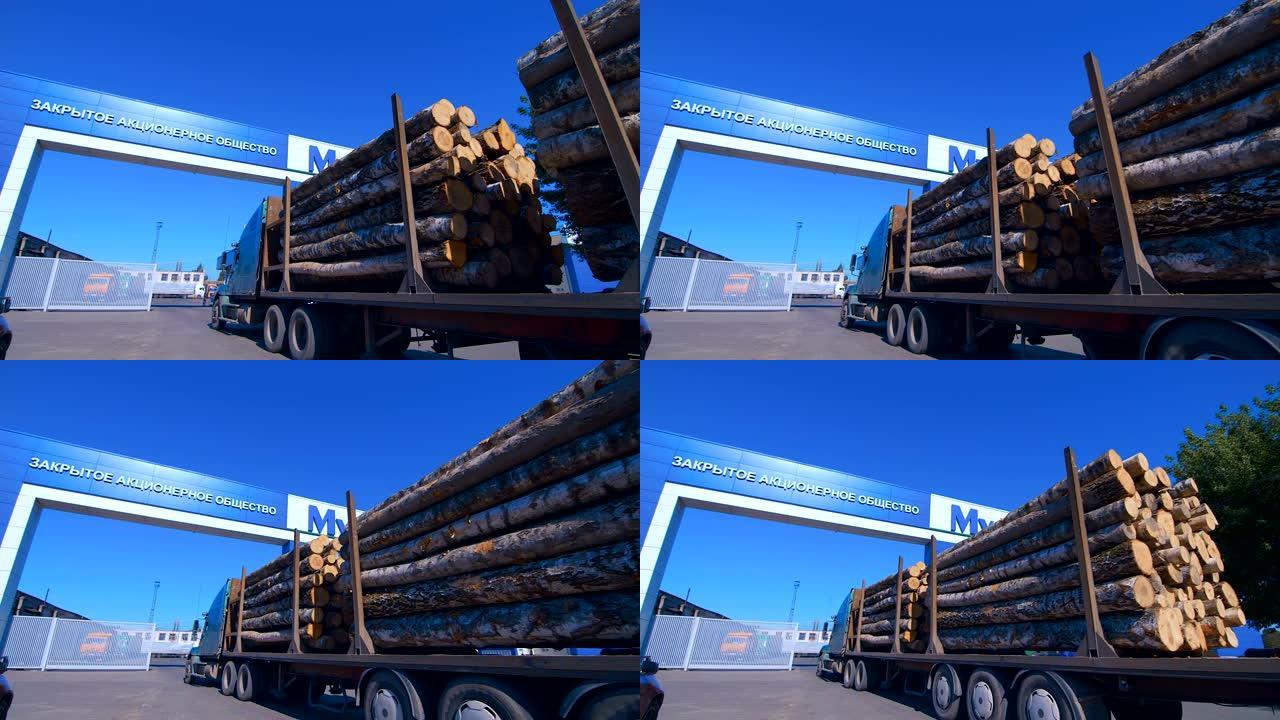 一辆装有拖车的木材卡车满载着原木，从木工厂区的入口驶入