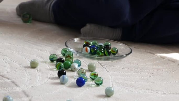 一个婴儿在地毯上玩玻璃弹珠和弹珠，彩色玻璃球和弹珠，