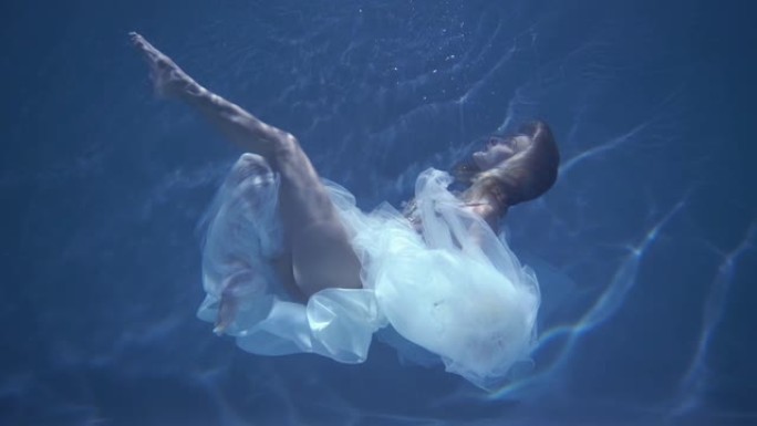 穿着白色连衣裙的长发女孩漂浮在水下