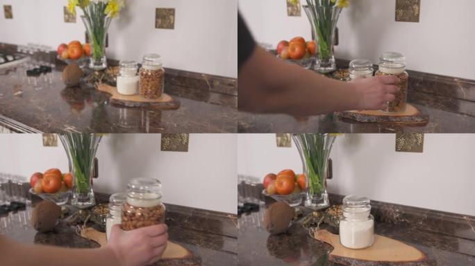 一个女人从大理石厨房台面上拿一个装满杏仁坚果的玻璃罐。摄像机关闭镜头。