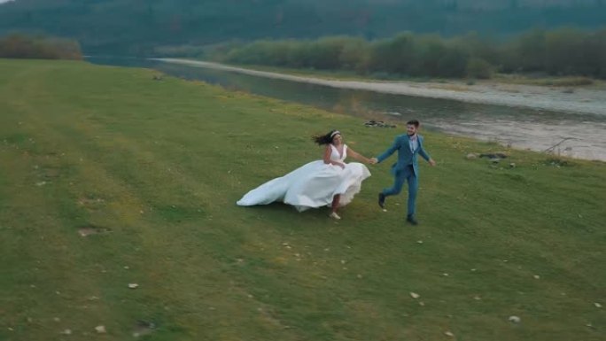 结婚夫妇在山河附近奔跑。新郎和新娘。Arial视图