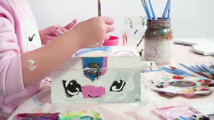 小女孩在木箱上画了一只白色独角兽和丙烯酸涂料。