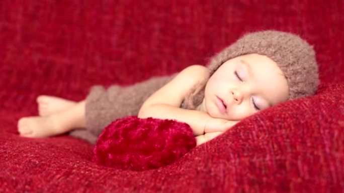 可爱的蹒跚学步的小男孩，带着心形玩具睡觉，可爱的针织衣服，孤僻