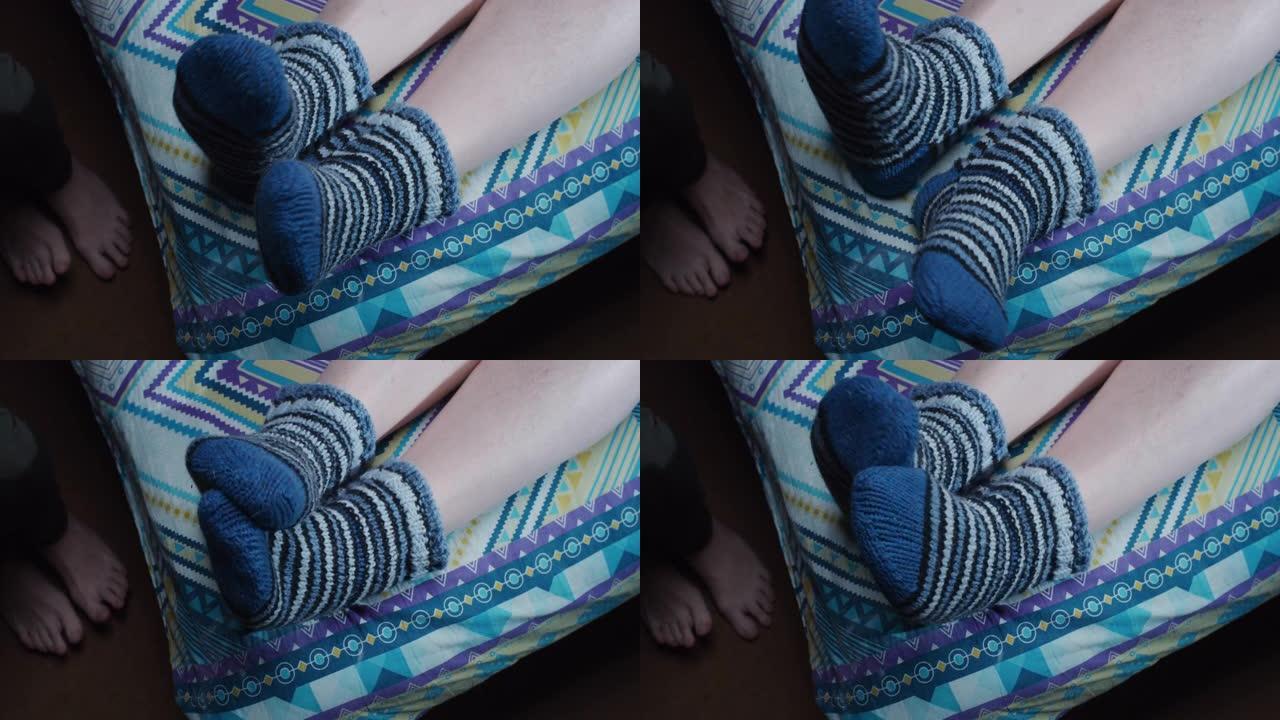 一双脚穿着羊毛袜子在床上活动，另一双脚赤脚站在地板上