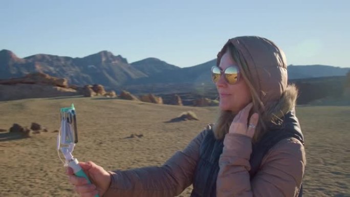 漂亮女孩在寒冷多风的天气里对着火星火山熔岩的风景自拍，并通过社交媒体分享