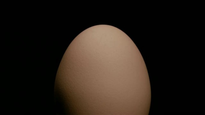 特写，整个半暗度的棕色鸡蛋在黑色背景上的转盘上旋转，直立位置