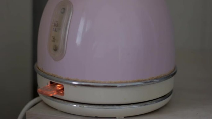 按下按钮打开桌上有水的旧电热水壶。煮沸并关闭水壶