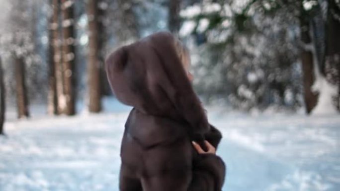 穿着兜帽皮大衣的顽皮女人微笑着在冬季自然森林散步。4k龙红相机