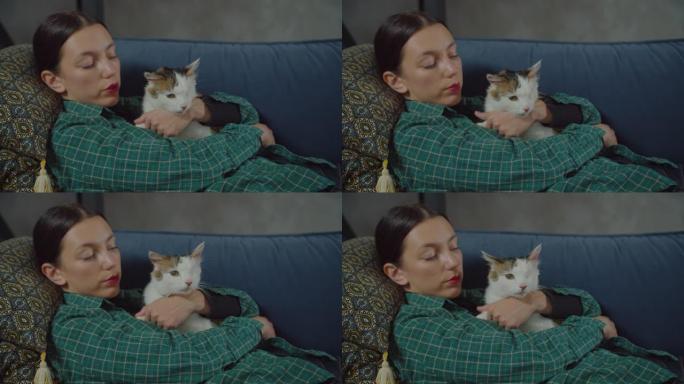 放松的漂亮女人在沙发上拥抱呼呼的猫