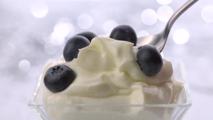 在银色的bokeh节日背景上拿一勺鲜奶油和蓝莓