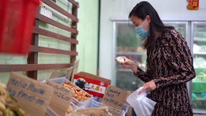 年轻的亚洲妇女戴着保护面罩在超市购买大蒜