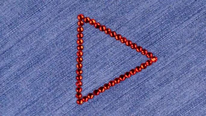 在牛仔布上旋转由红色水钻制成的三角形，该三角形象征着完成。