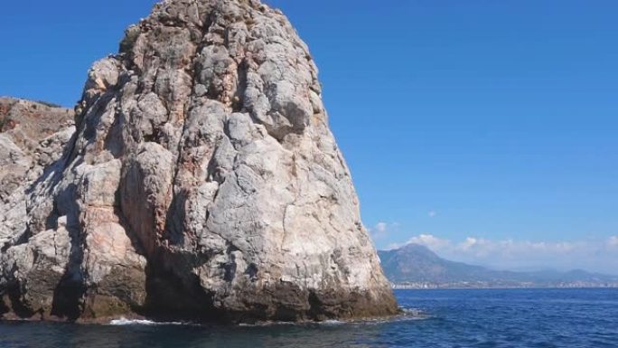 在海岸和蓝色的翡翠海的背景下，风景如画的岩石特写镜头。一条石帆，一座山，一块岩石从大海深处升起