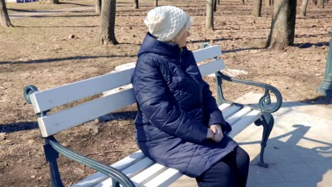 阳光明媚的早春，一个孤独的沮丧的老年妇女坐在城市公园的长凳上的肖像-冷漠，抑郁和老年人的心理概念