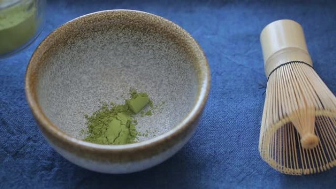 男子在蓝色表面的碗里准备绿茶抹茶。饮料是抗氧化剂和多酚的丰富来源。