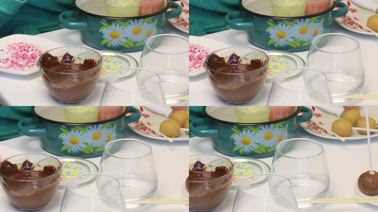 盘子上有彩色的popcake调味料，旁边的桌子上放着带有糖霜的玻璃杯。盘子上是粘着棍子的饼干球。