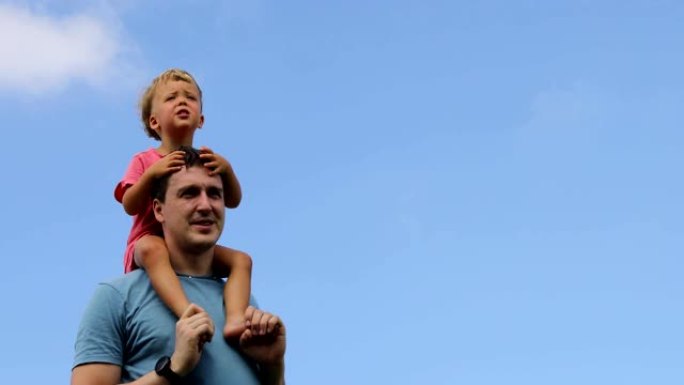 孩子坐在父亲的肩膀上，面对蓝天