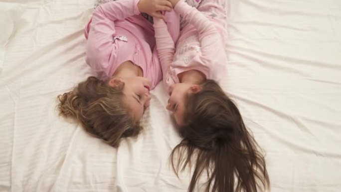 穿着粉红色睡衣的小女孩倒立躺在床上，微笑着互相拥抱