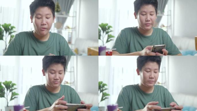 快乐的亚洲男孩在家里的窗户附近通过智能手机玩网络游戏，生活方式概念。
