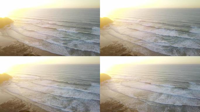 飞掠海滩的鸟瞰图，海浪逼近，日落时白色喷雾