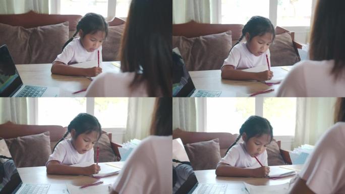 亚洲女学生在做作业，而母亲在家工作。由于Covid 19大流行，孩子在检疫期间在家上学，父母在家用笔