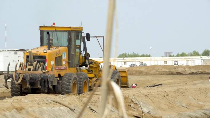 一个挖土机在工作 水泥地上停了很多挖土机和卡车 一群人在绑钢筋