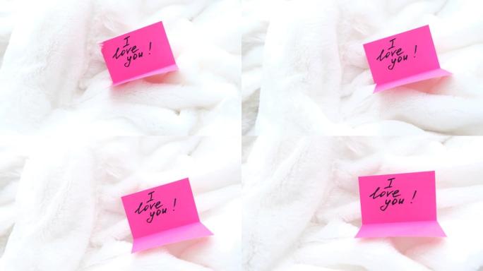 爱的宣言，感人的信息我爱你在白色蓬松毯子上的粉红色明信片上。舒适卧室的细节，爱人的早晨