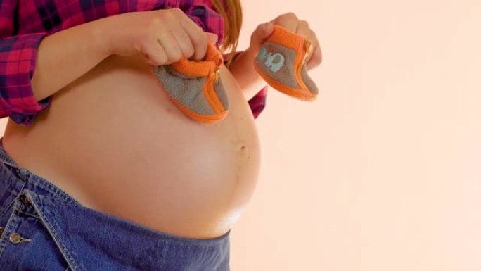 展示婴儿短靴的女性手。在母亲手中为新生男孩关闭手工婴儿短靴。儿童鞋。怀孕概念。中枪