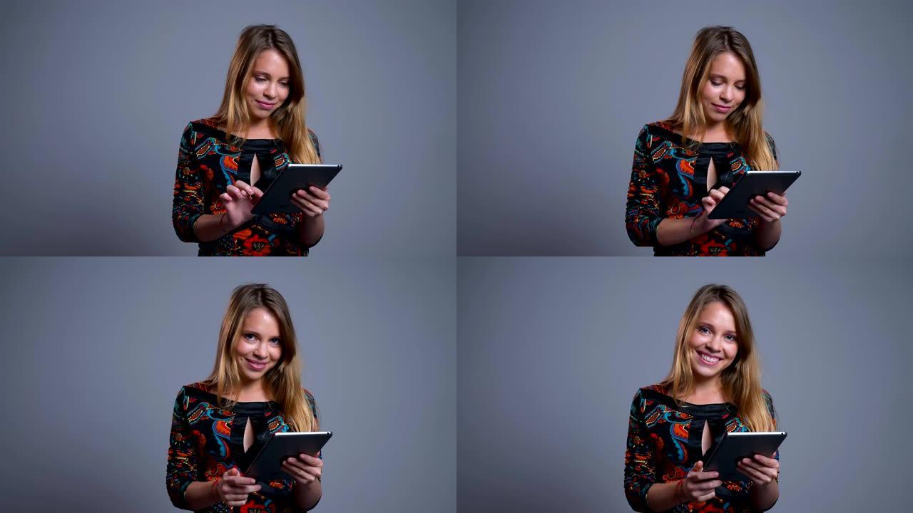 迷人的年轻高加索女性在平板电脑上滚动的特写肖像看着相机并大笑