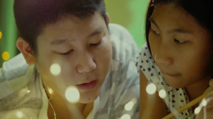 快乐的亚洲男孩和他的妹妹在晚上一起在床上看书。生活方式概念。