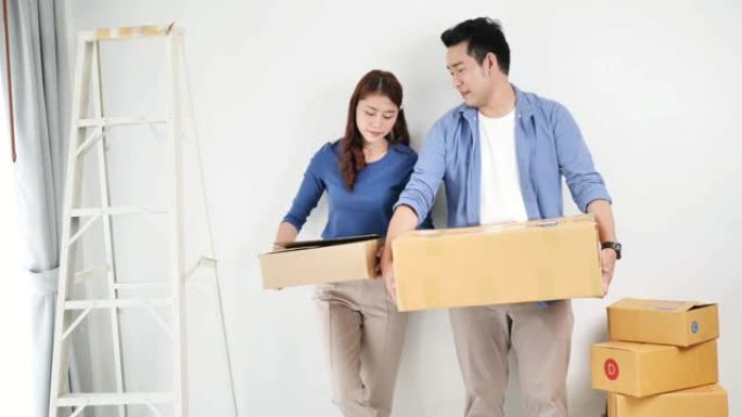 幸福的亚洲夫妇拿着棕色的盒子搬到新房子，生活风格的概念。