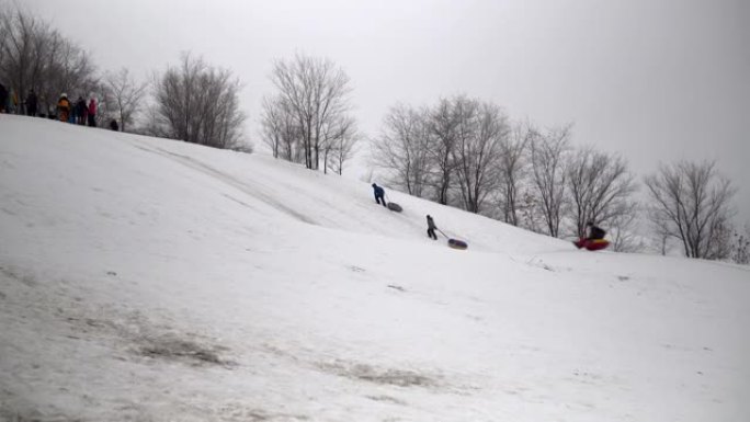 一群人骑在雪地滑梯上。孩子们在充气环上的冰滑梯上列出自己。雪橇、塑料溜冰场