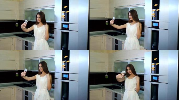 一个穿着白色连衣裙的年轻女孩在家在现代厨房里自拍。