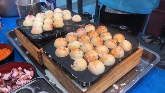 厨师手从章鱼烧锅中拿起日本休闲食品章鱼烧到盒子里，以便在日本街头食品市场的夏季节日中出售。男子烹饪什