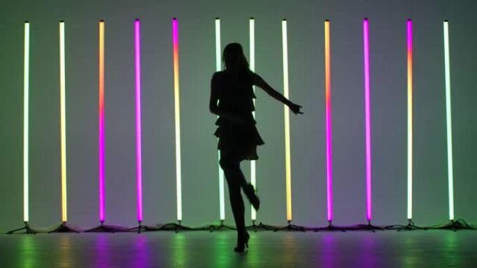 一位年轻女子在多色霓虹灯的背景下，在工作室中展示了伦巴舞的元素。慢动作中充满激情的拉丁美洲舞蹈
