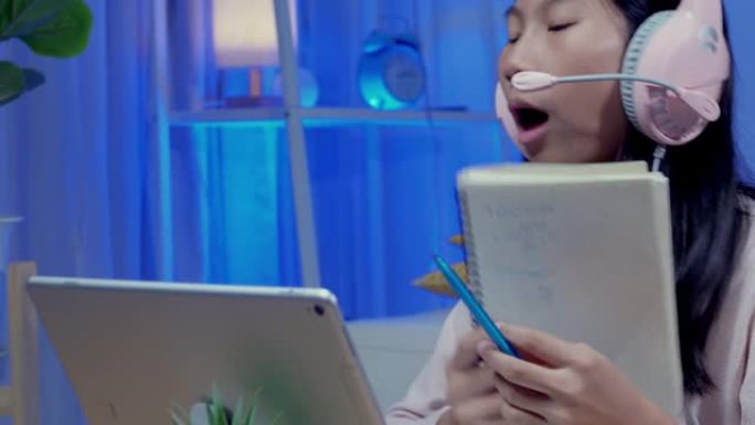 亚洲女孩戴着带麦克风和数字平板电脑的耳机，在新型冠状病毒肺炎期间与老师和朋友在家上学，社交距离和新的