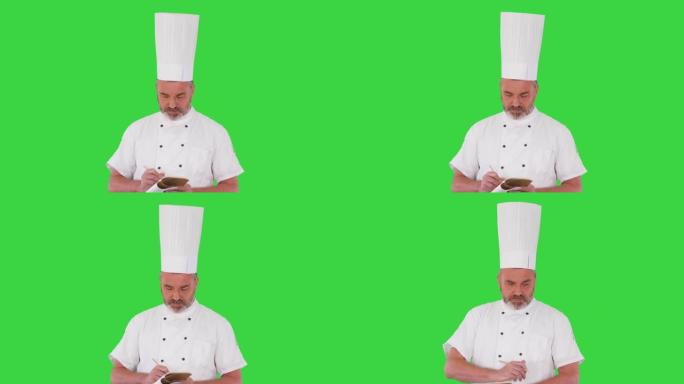 高级男厨师在绿屏上做笔记，色键