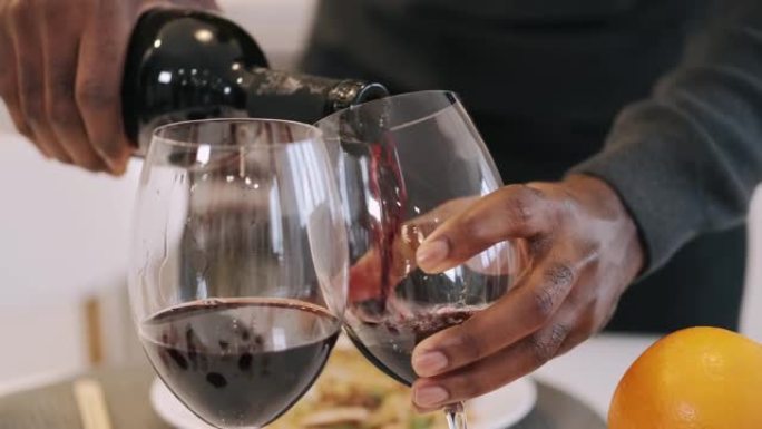 非裔美国人将葡萄酒倒入浪漫晚餐的玻璃杯中